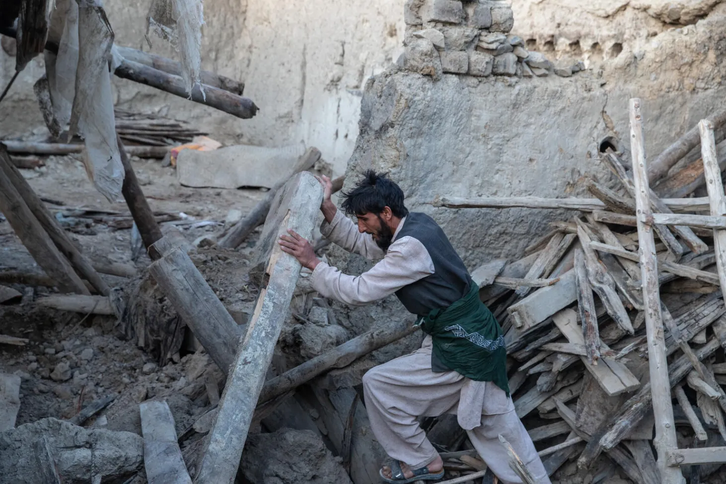 A man pushes a wooden column up in the rubble of a home
