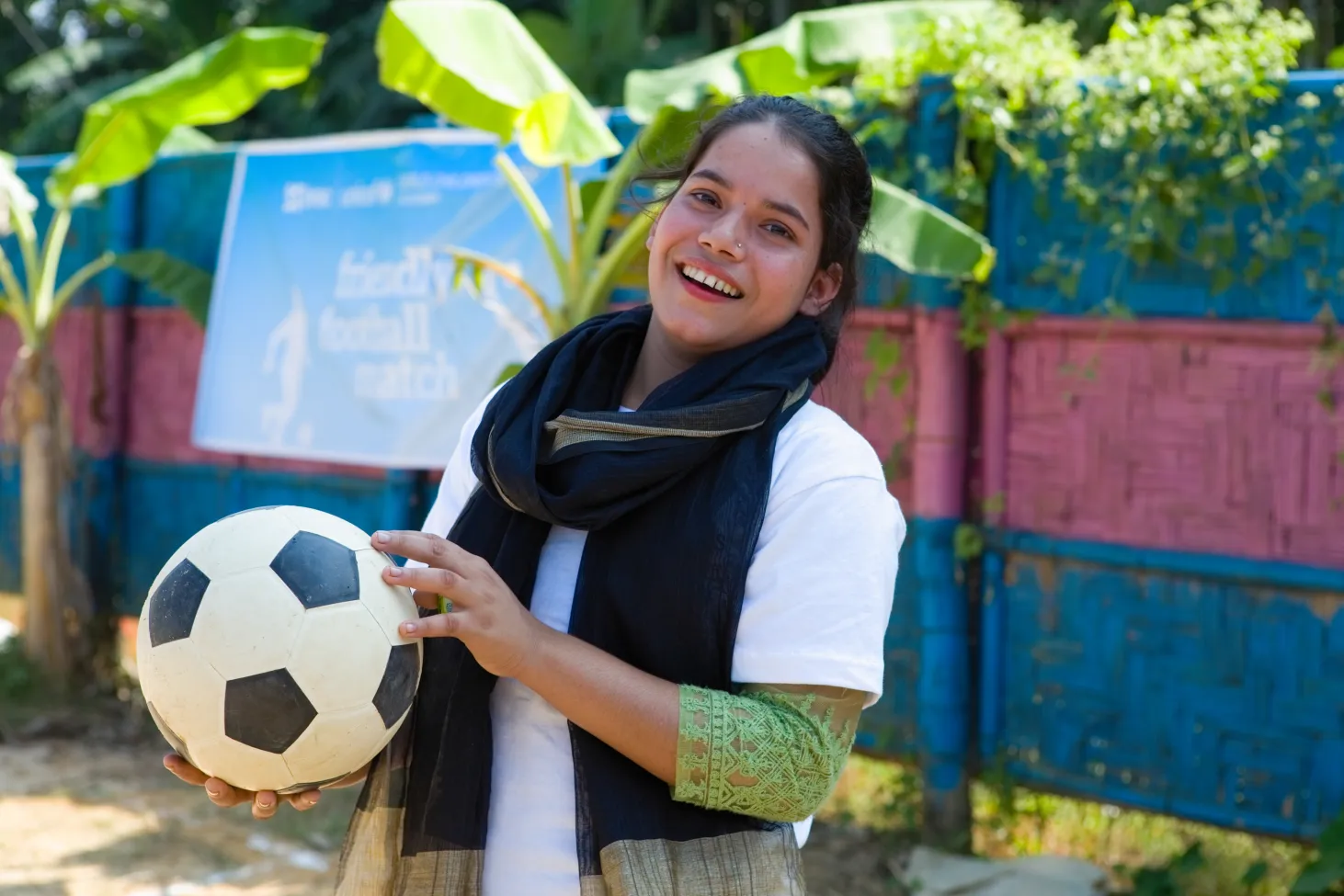 An adolescent girl holds a soccer ball and smiles while looking at the camera. 