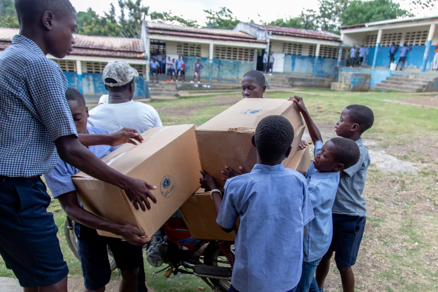 Les élèves déchargent des cartons de kits scolaires d’une moto pour la distribution à l'École Nationale de Jorgues.