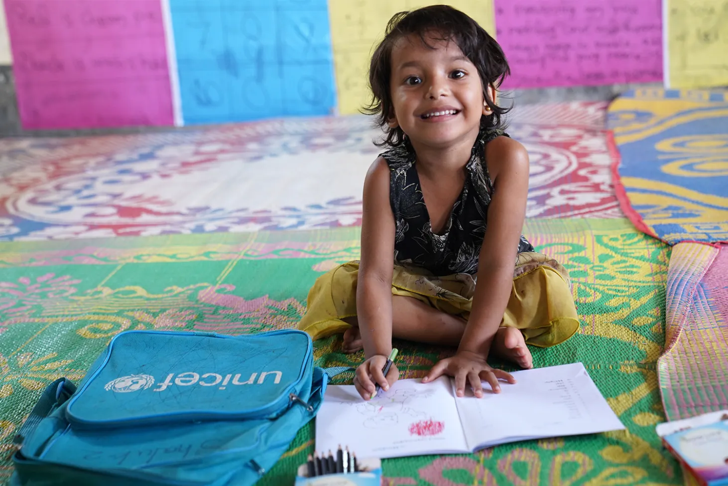 Une fillette assise au sol dessine dans un jardin d’enfants soutenu par l’UNICEF dans un camp de réfugiés rohingyas.