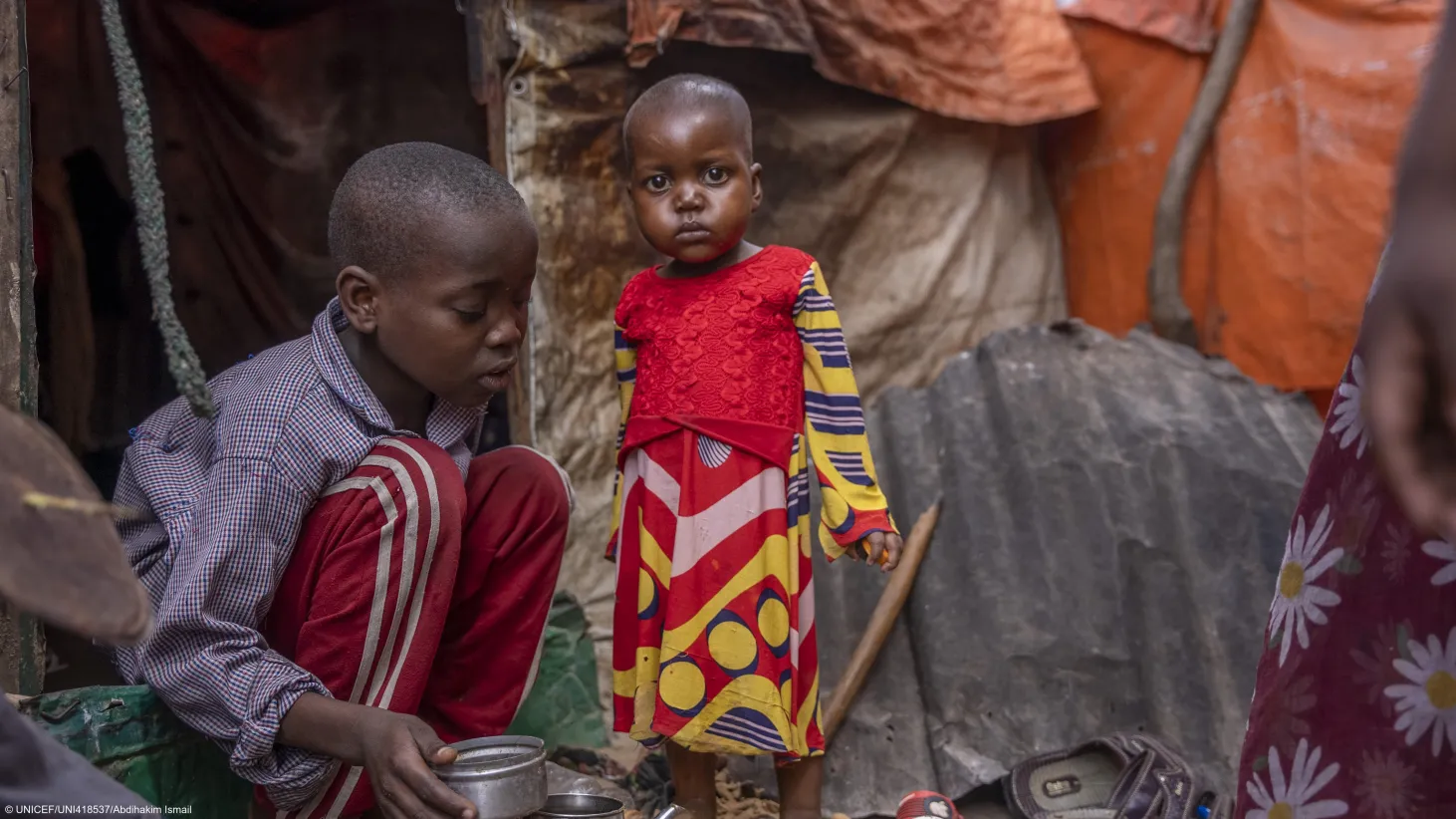 Une petite fille joue avec son frère devant leur tente dans un camp pour personnes déplacées à l’intérieur du pays en périphérie de Mogadishu, en Somalie. 