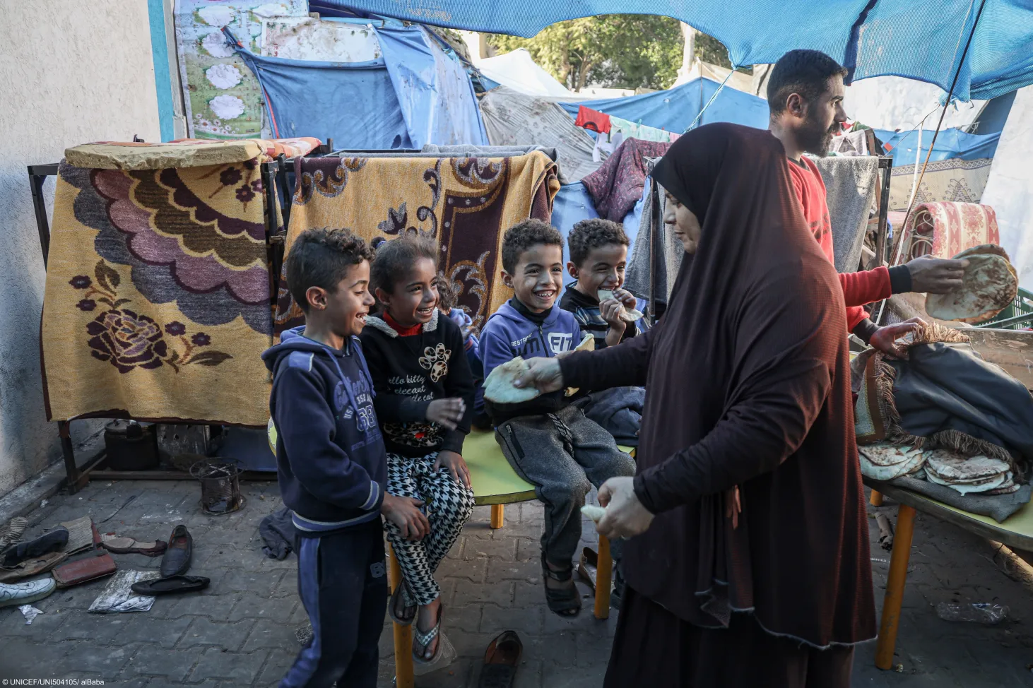 Mohammed's grandmother hands a piece of flatbread to 9-year-old Dalia, Mohammed's sister, as she sits next to Mohammed (left) and twin brothers Salah and Ameer outside their family's makeshift tent in a shelter for internally displaced persons in Rafah, southern Gaza Strip.