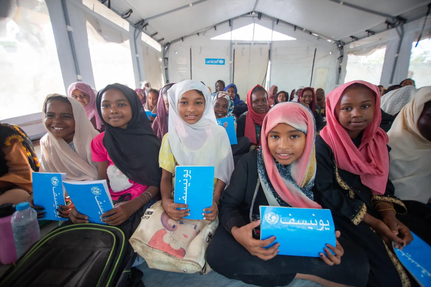 Des enfants munis de cahiers bleus de l’UNICEF sourient à l’objectif dans un espace d’apprentissage sûr soutenu par l’organisme dans l’État de Gezira, au Soudan.