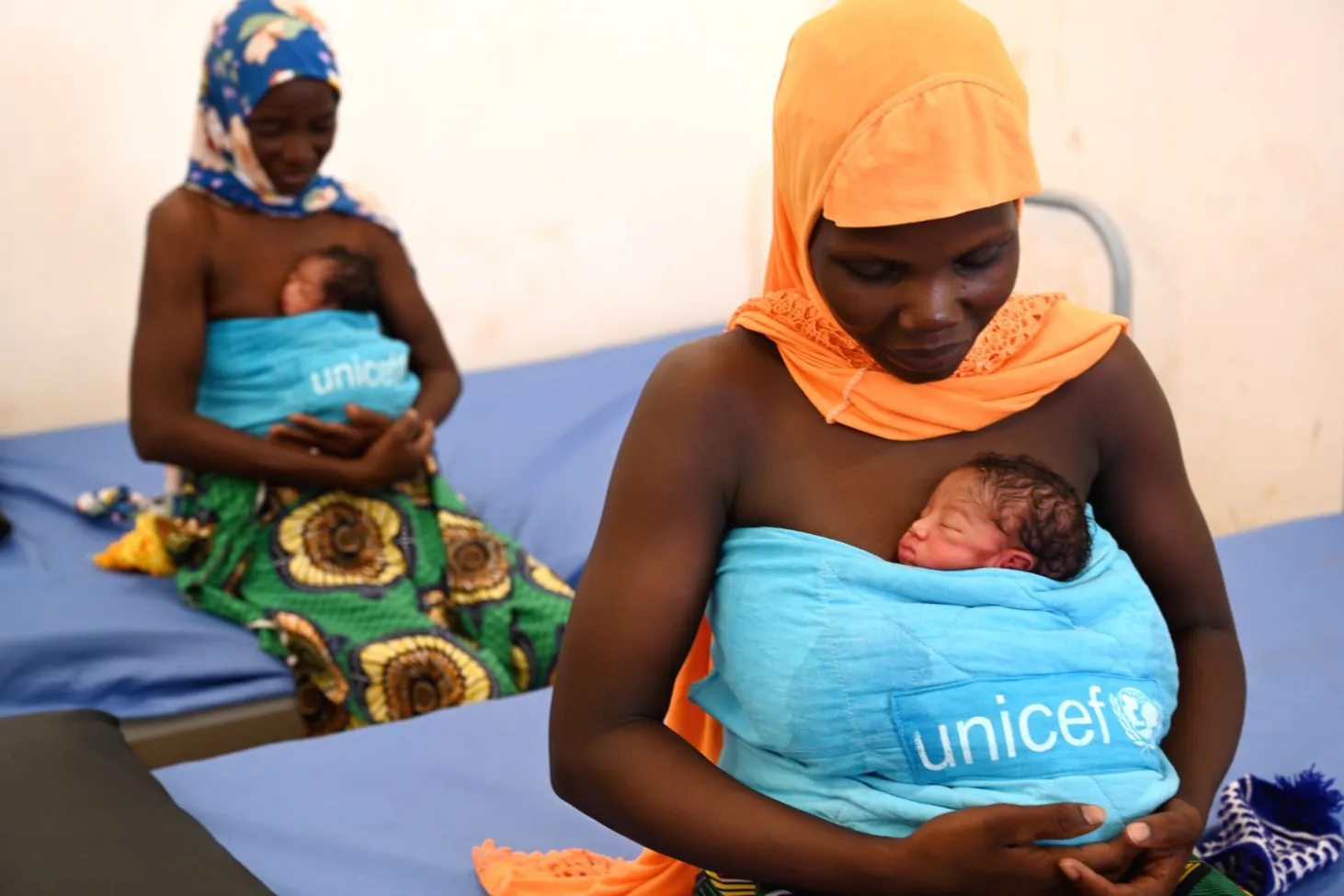 Dans un hôpital du Burkina Faso, deux mères tiennent contre leur poitrine leur bébé enveloppé dans une couverture de l’UNICEF. 