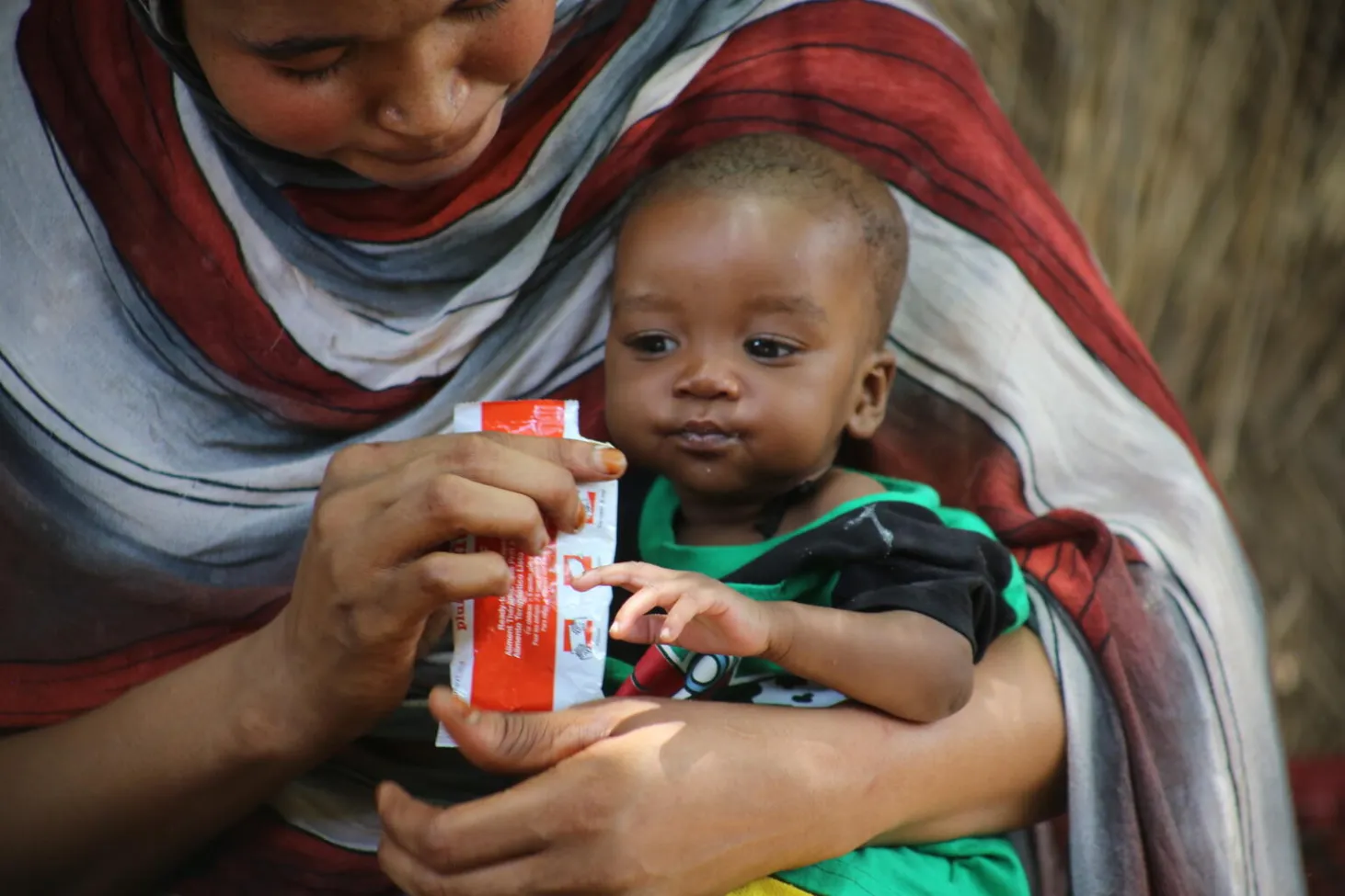 A baby is being fed a packet of ready-to-use therapeutic food by his mother. 