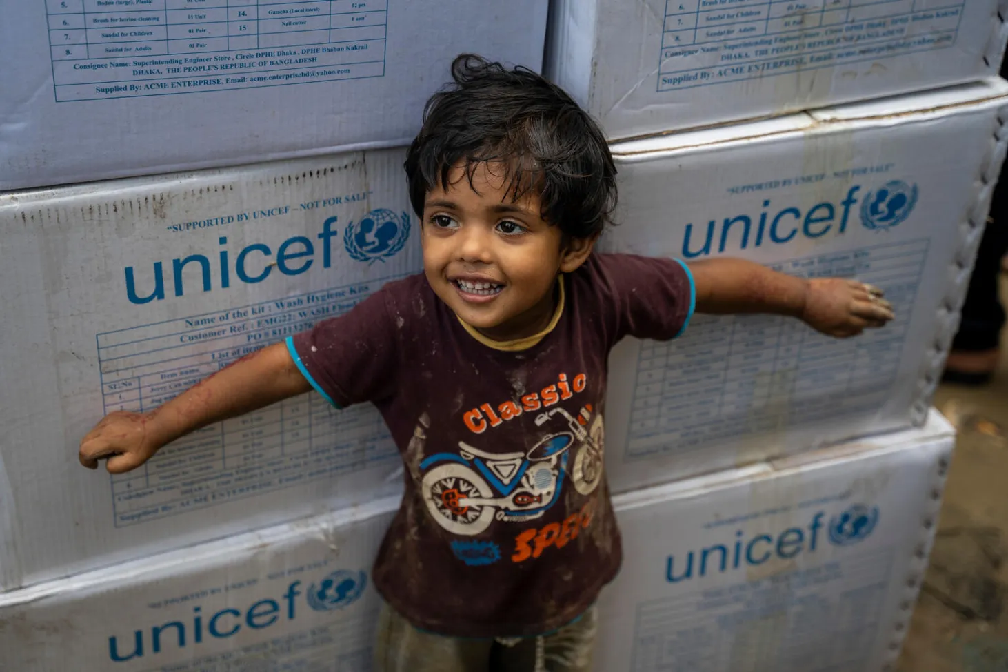 Un enfant se tient devant des boîtes blanches de l’UNICEF.