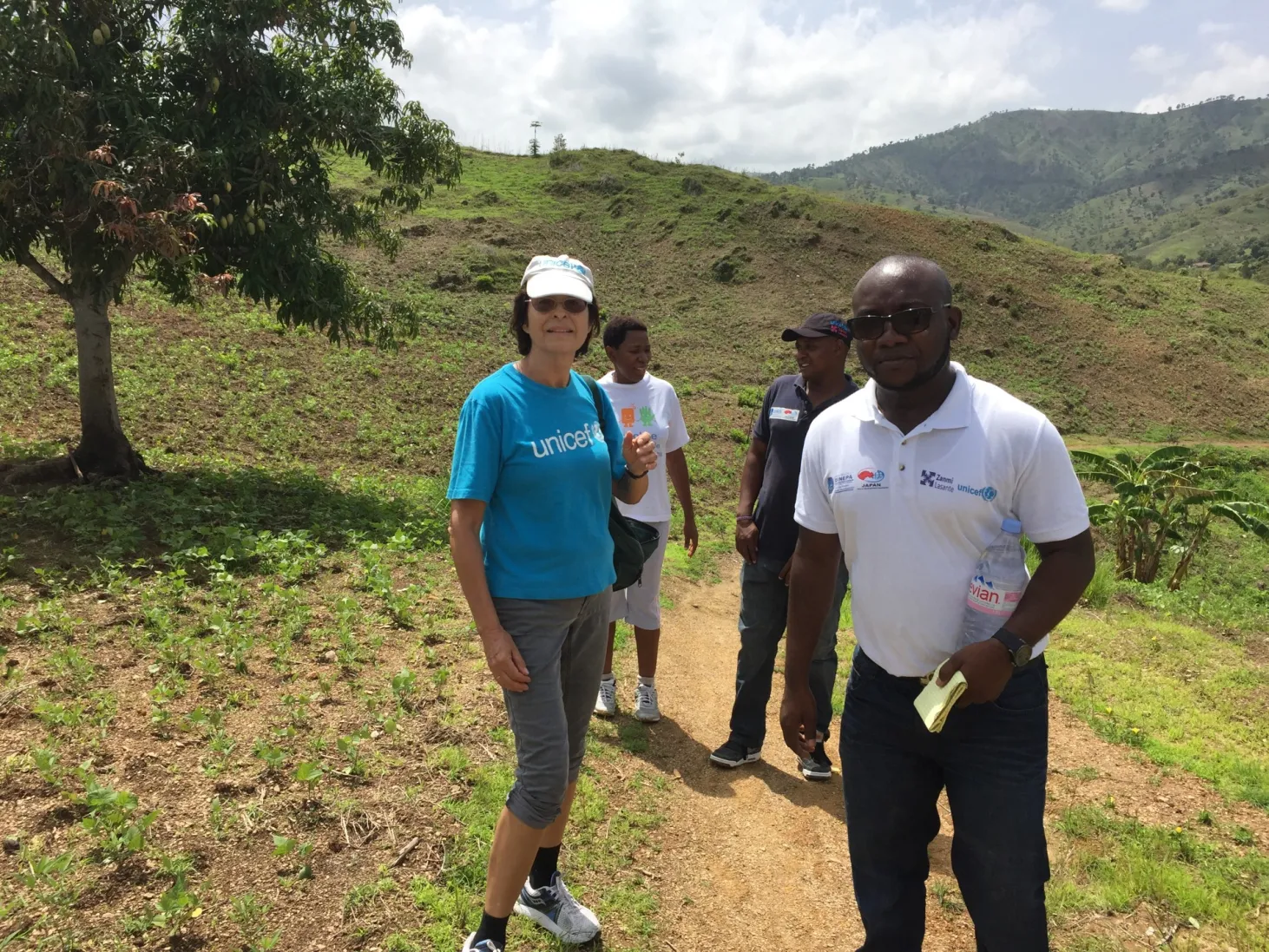 Susana with two other people stand on a dirt path on a sunny day in a hilly, grassy landscape.