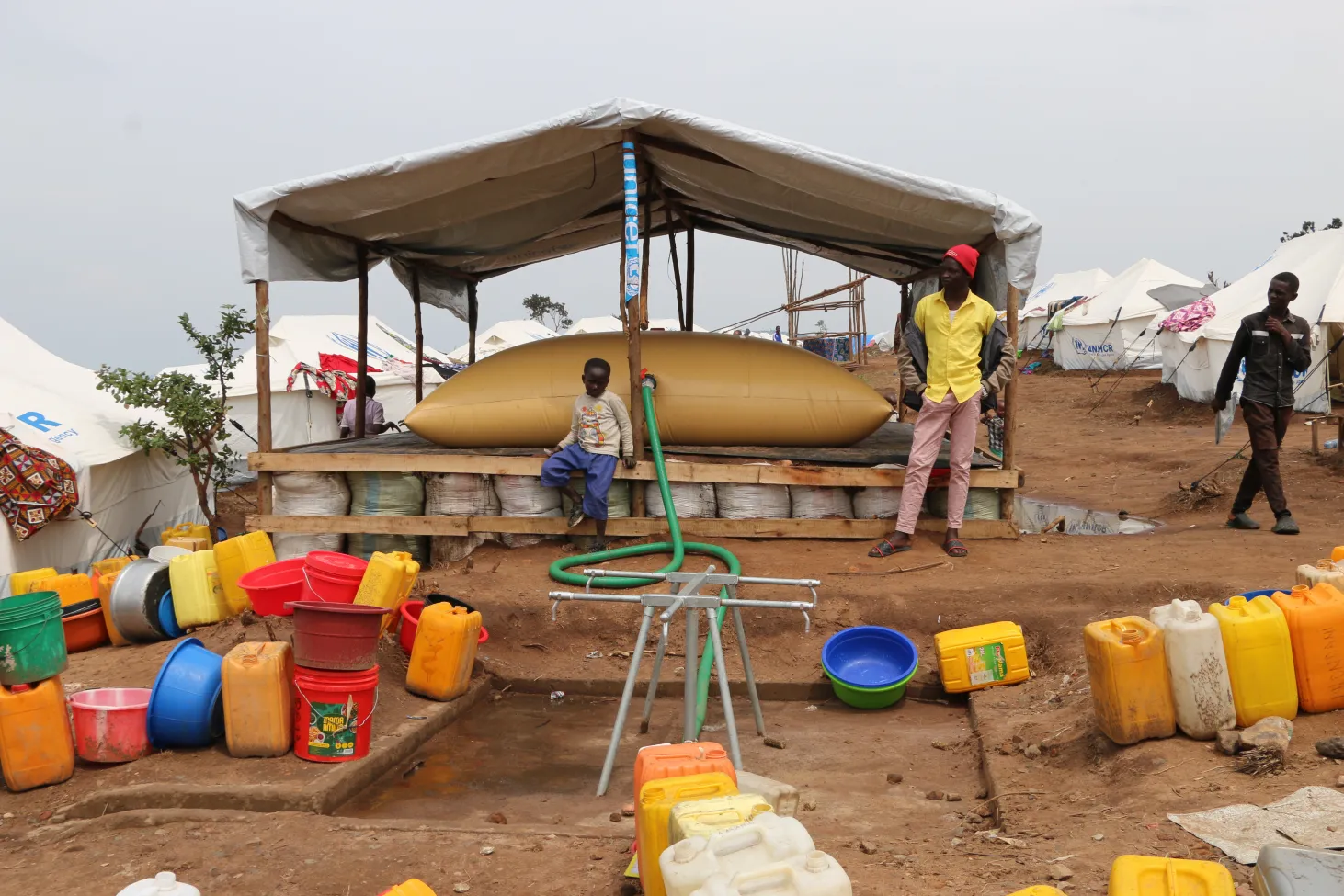 Point d’accès à de l’eau potable, avec réservoir surélevé, robinet sur pied et de nombreux conteneurs de collecte pour l’approvisionnement en eau de la communauté.