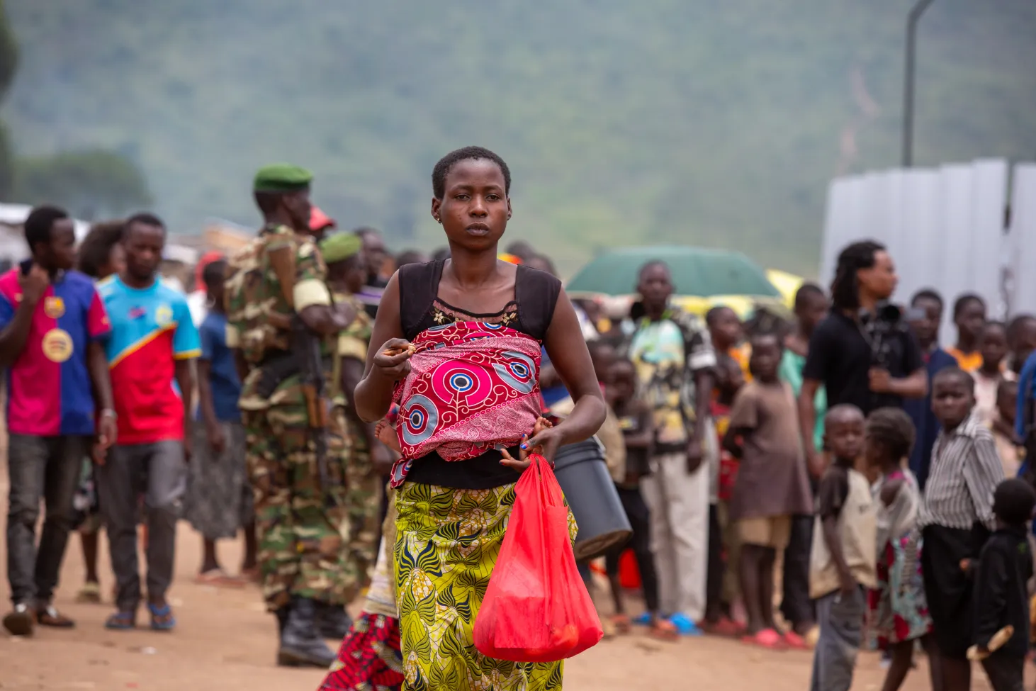 Une femme portant un bébé marche sur un chemin bondé.