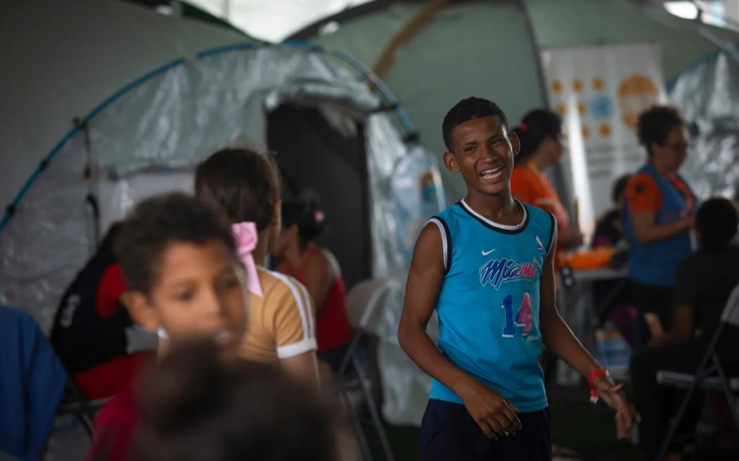 At a temporary camp, a boy wearing blue laughs among other children.  