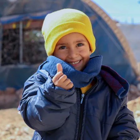 En Syrie, Rashid, âgé de quatre ans, sourit et lève le pouce en portant ses nouveaux vêtements d’hiver distribués par l’UNICEF dans le camp de Fafin pour les familles déplacées.