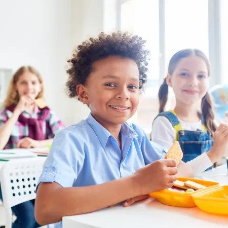 Three children in a classroom eating lunch at their desks.