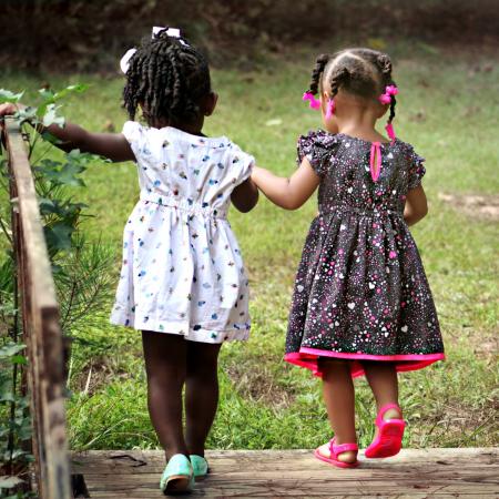 Two girls, holding hands, walk across a bridge.