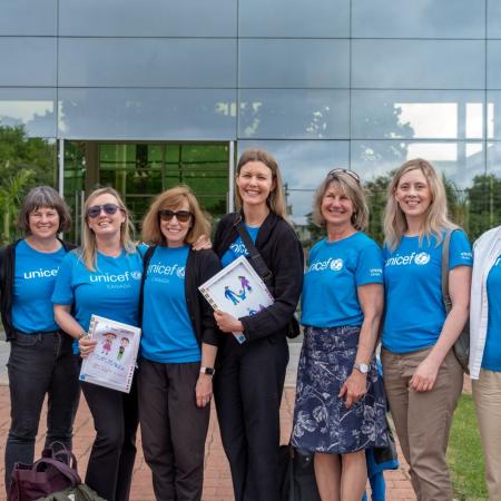 A group of women wearing blue UNICEF shirts smile at the camera. 