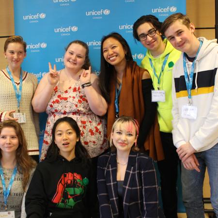 Eight children stand in front of a UNICEF Canada sign, they are all wearing UNICEF lanyards. This photo was taken in Toronto, Canada in 2019. 