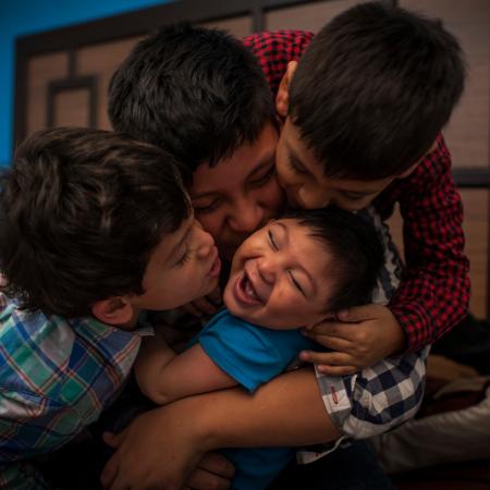 A boy laughs as his brothers shower him with kisses. Help UNICEF Support Right to a Childhood.