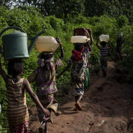 Children walk along a path in the forest, carrying buckets atop their heads, to gather water from a natural spring at Elevage IDP camp in Bambari, Central African Republic