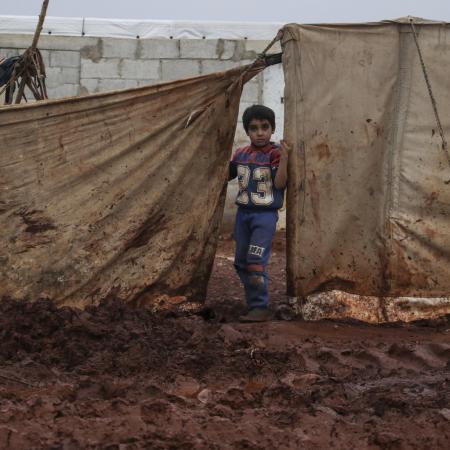 Young boy stands near the tent where he lives with his family, Atma camp, Idlib