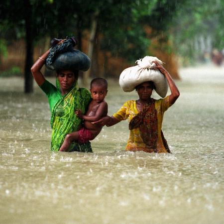 Two women and a small child wade through floodwaters in Bangladesh.