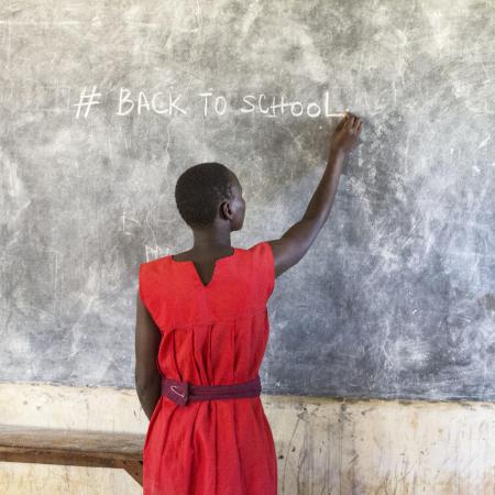 A girl writes on a chalkboard in a classroom in Uganda.