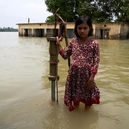 A little girl stands near a flooded water pump in India.
