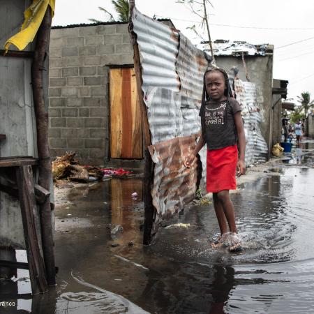A girl walks through an inundated street in a slum-like setting, with the walls of some homes destroyed. This photo was taken in Mozambique. 