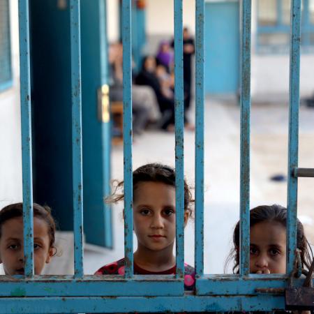 Three girls peeking outside a gate at one of 29 UNRWA schools used as temporary shelter.