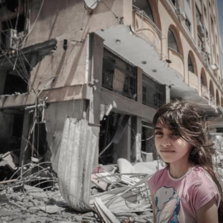 On 17 May 2021, a Palestinian girl stands in front of their home as her family extracts their possessions from inside their damaged home after being targeted in Gaza City.