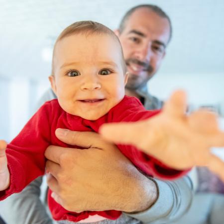 Toddler being held by his father reaches for the camera