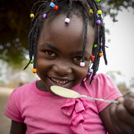 A child smiles as she eats a meal at the school in Mbuene village, Magude district, Maputo Province, Mozambique