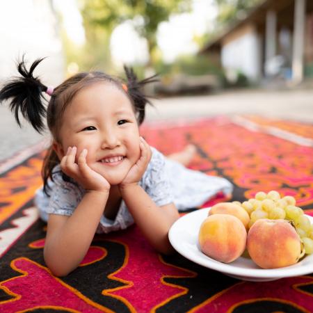 A little girl poses with a bowl of fresh fruits.