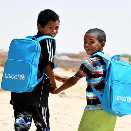 In north Niger, two children laugh and walk together while wearing their new UNICEF school backpacks filled with classroom supplies.
