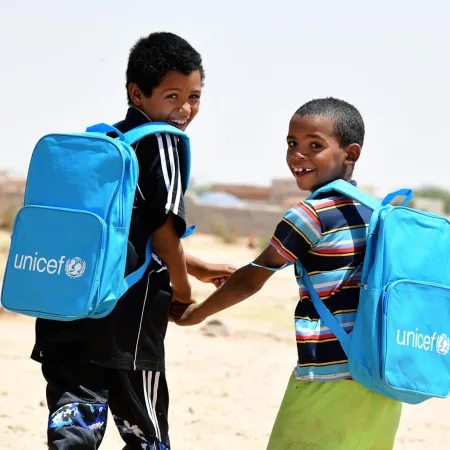 Dans le nord du Niger, deux enfants rient et marchent ensemble en portant leurs nouveaux sacs à dos de l’UNICEF remplis de fournitures scolaires.