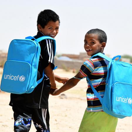Dans le nord du Niger, deux enfants rient et marchent ensemble en portant leurs nouveaux sacs à dos de l’UNICEF remplis de fournitures scolaires.