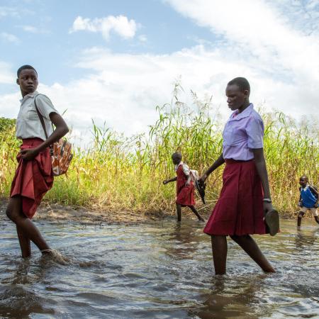 Students walking on foot across flooded paths - South Sudan