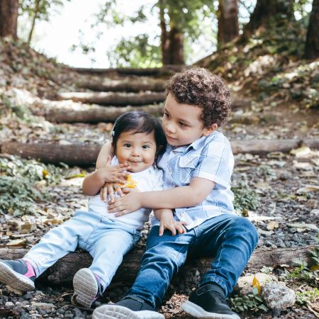 Older child hugging toddler on a nature path