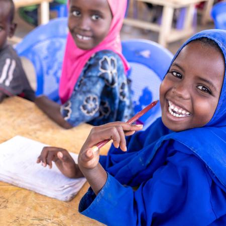 De jeunes élèves rient en faisant leurs devoirs ensemble à une table dans une classe d’une école primaire de Dolow, en Somalie.