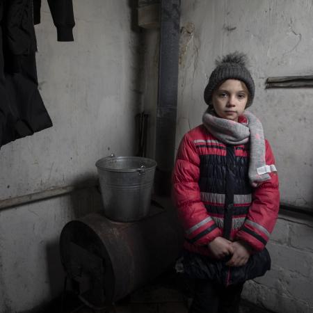En Ukraine, une fille portant des vêtements d’hiver se tient à côté d’un poêle à bois.