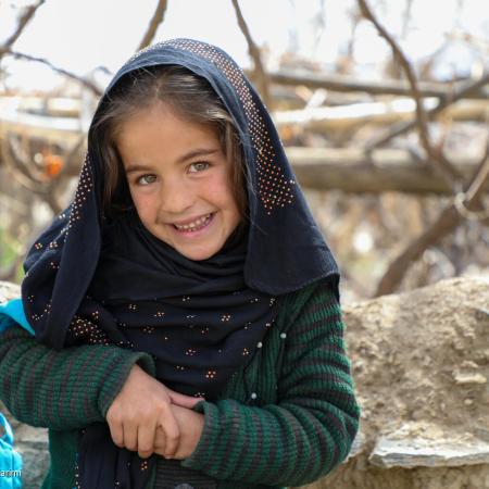 En Afghanistan, une jeune fille sourit à la caméra, la sangle bleue d’un sac à dos de l’UNICEF sur le bras.