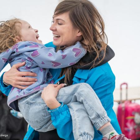 A woman holds up a child in her arms, the child is laughing. The woman is also smiling and wearing a blue UNICEF jacket. This photo was taken in Romania is 2022. 