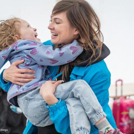 A woman wearing a blue UNICEF jacket holds a child in her arms, both are laughing. This photo was taken in Romania. 