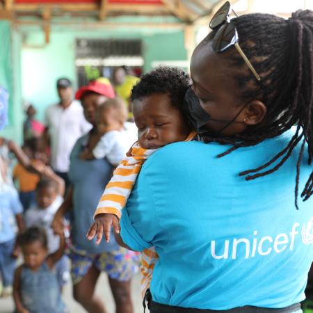 En Haïti, un membre du personnel humanitaire de l’UNICEF porte un enfant âgé de trois mois.