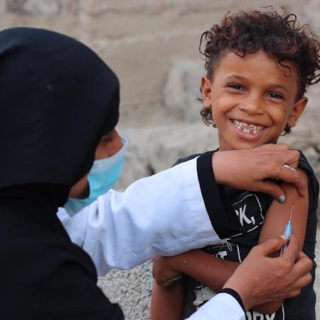 Young child smiling at camera while getting vaccinated in Yemen.