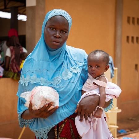 a woman in a blue scarf holding a packet of food in one hand and a child in the other. 
