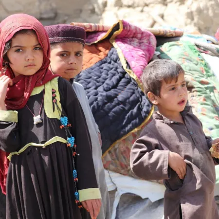 Trois frères et sœurs se tiennent devant leur maison détruite.