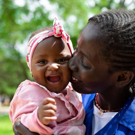 A baby smiles at the camera while being carried by her mother.