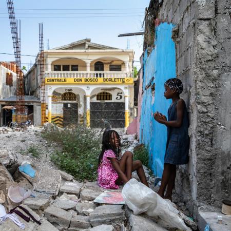 On 18 July 2022 in Les Cayes, Haiti, children play in the rubble of homes destroyed in the 2021 earthquake. The girl in blue lives nearby with her mother, Yolande Felix, and younger sister, Valentine.