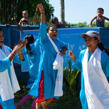 Three girls cheer on the sidelines of a soccer game in Bangladesh. 