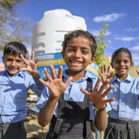 Three children showing their washed hands smile at the camera.