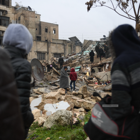 People gather around collapsed buildings as rescue teams look for survivors following an earthquake in the Syrian city of Aleppo